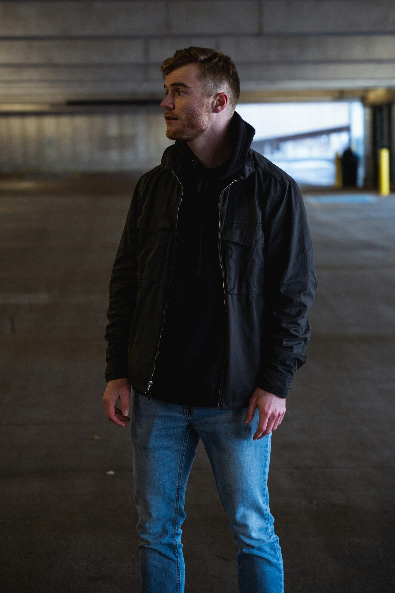 man in black leather jacket and blue denim jeans standing on sidewalk during daytime