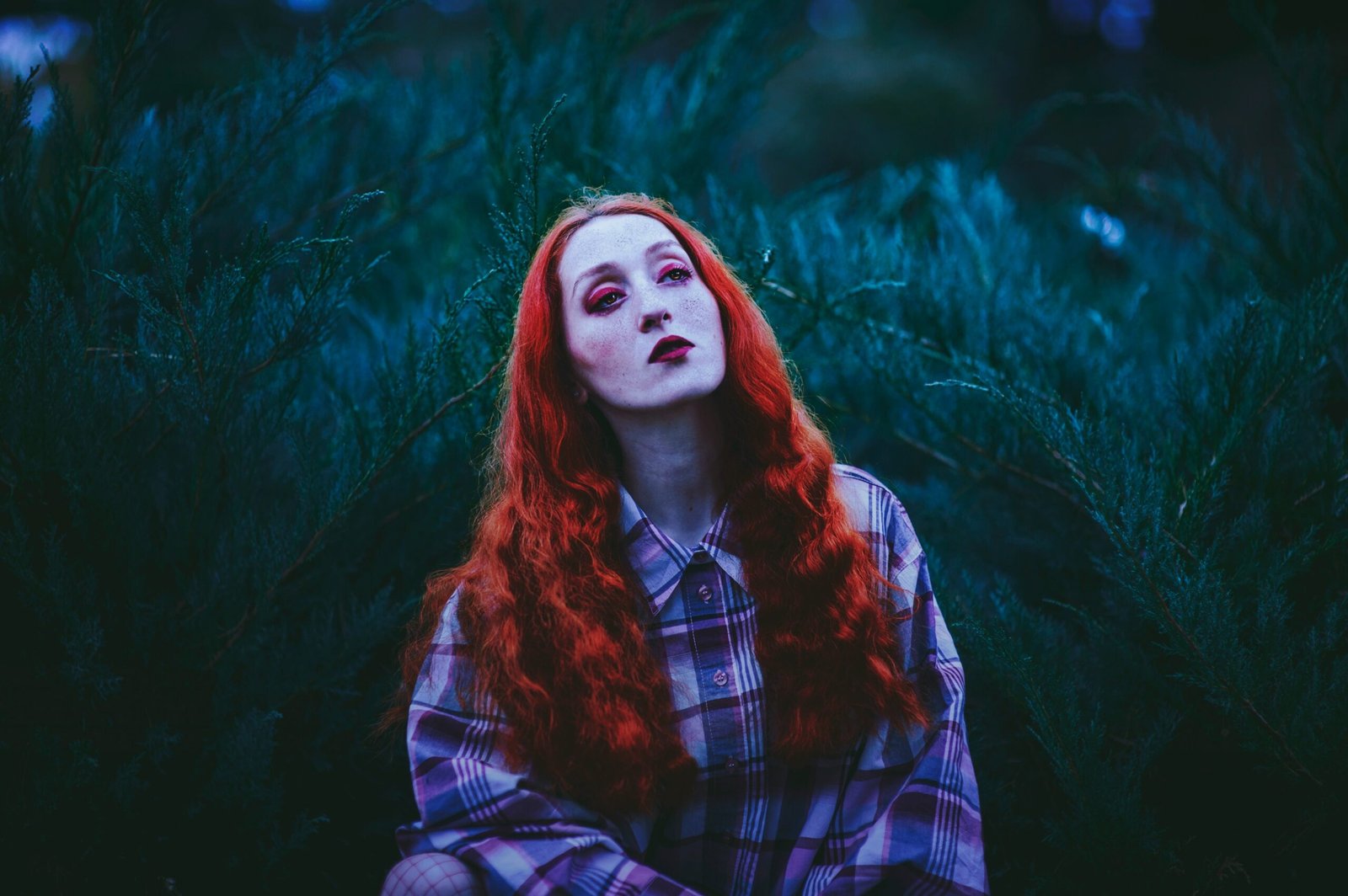 photography of red-haired woman standing near leafed plants